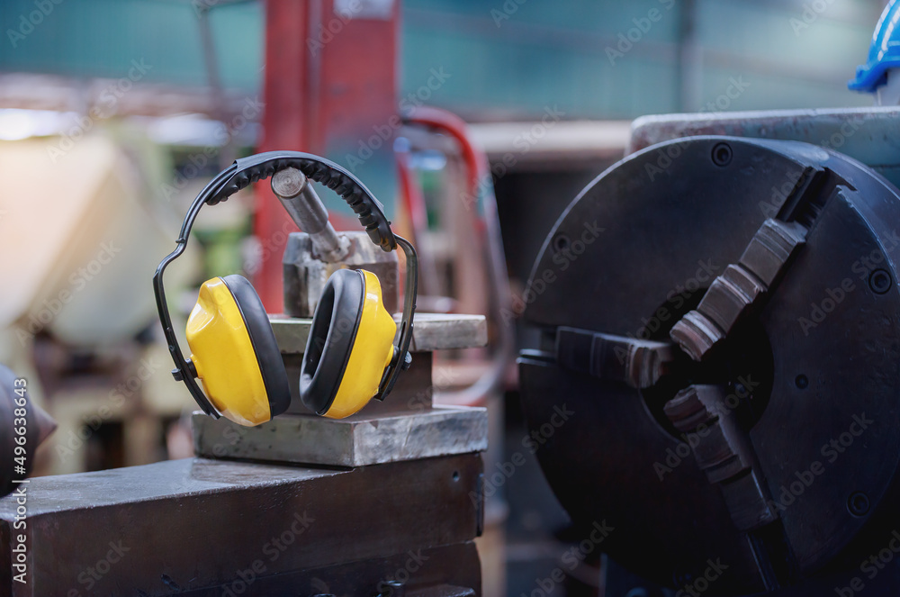 Yellow protective ear muffs hang on machines in heavy industrial plants. - obrazy, fototapety, plakaty 