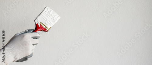 Paint brush, close up hand painter worker painting on surface wall Painting apartment, renovating with white color paint. Leave empty copy space to write descriptive text beside. photo
