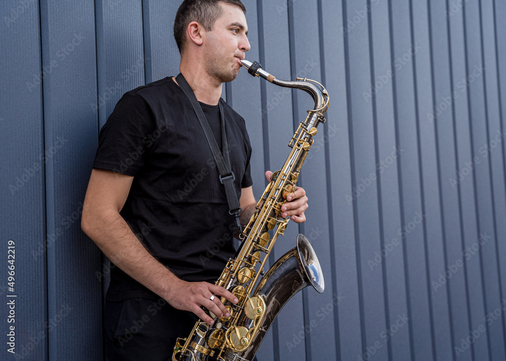 Fototapeta premium Young street musician playing saxophone near the big blue wall
