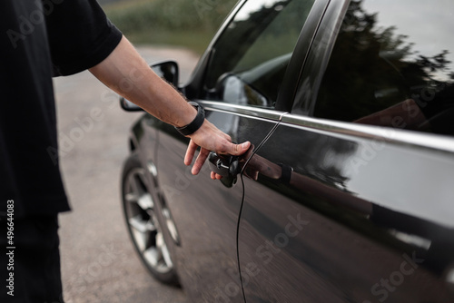 Man driver opens the door of a black car. A man's hand holds the door handle, close-up. Rent a car