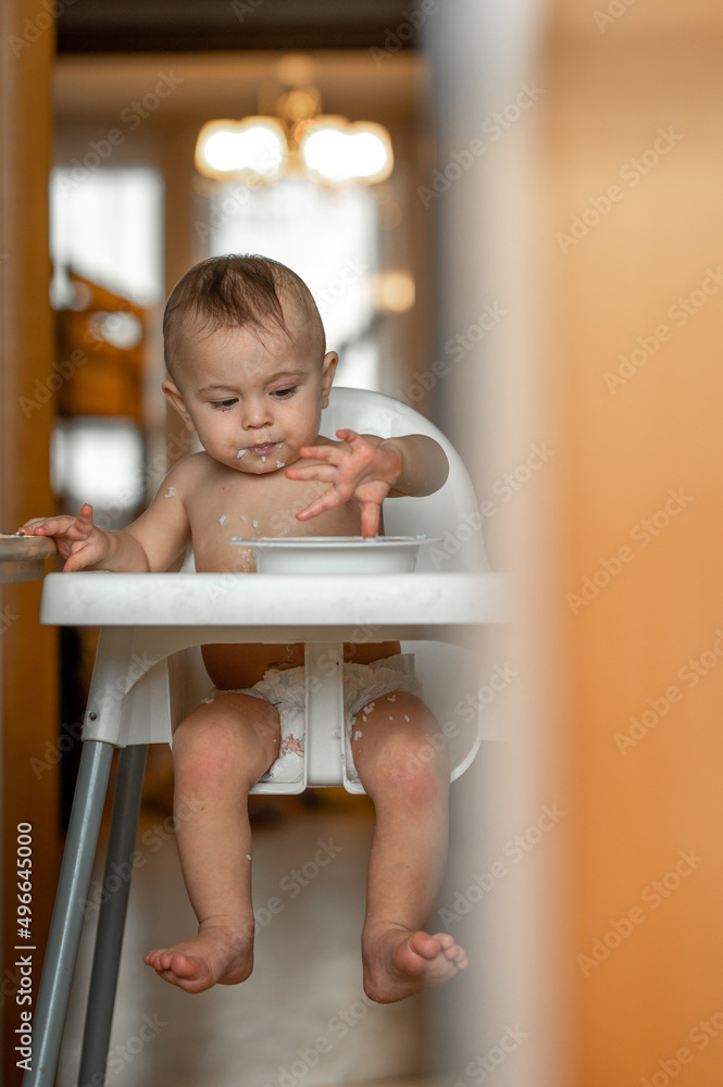 a little boy at home in the kitchen is sitting in a high chair having breakfast, he eats porridge a little boy at home in the kitchen is sitting in a high chair having breakfast, he eats porridge