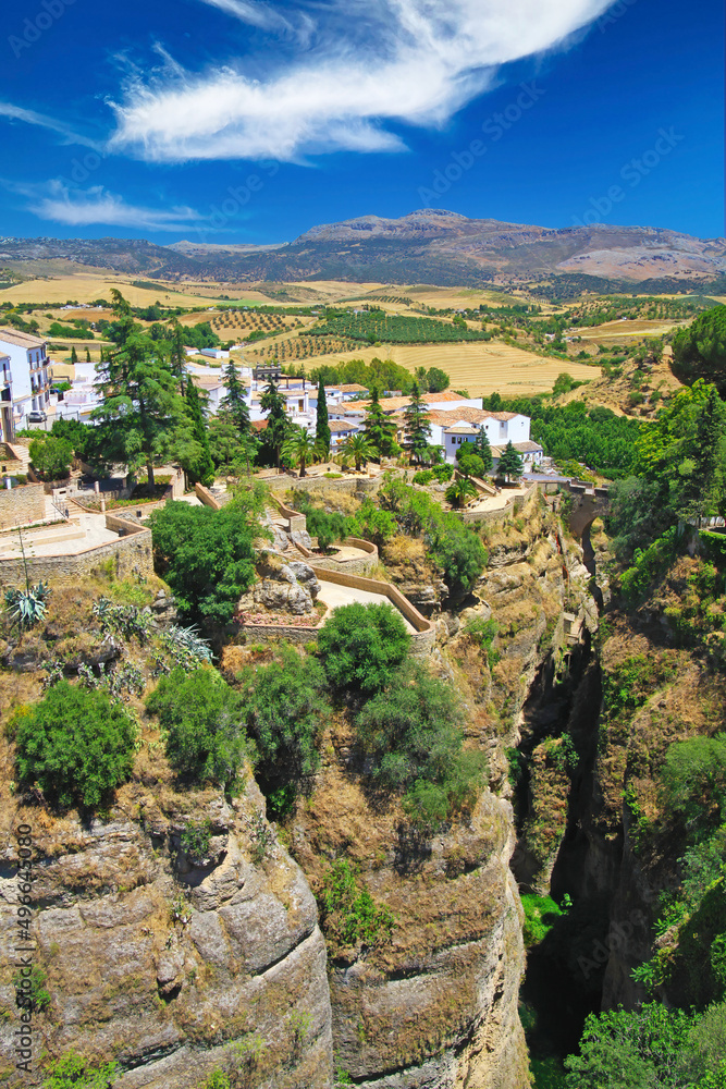 View on ancient village Ronda located precariously close to the edge of steep cliff, clear blue sky with fluffy cloud - Andalusia, Spain