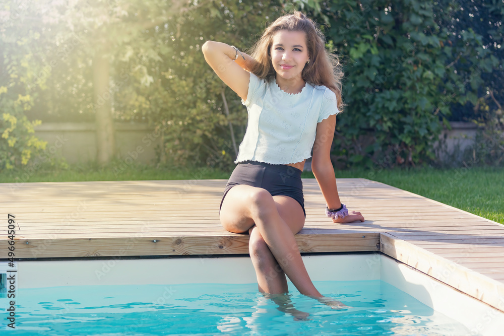 Cute tanned girl is sitting on the edge of the pool in the garden. Horizontally. 
