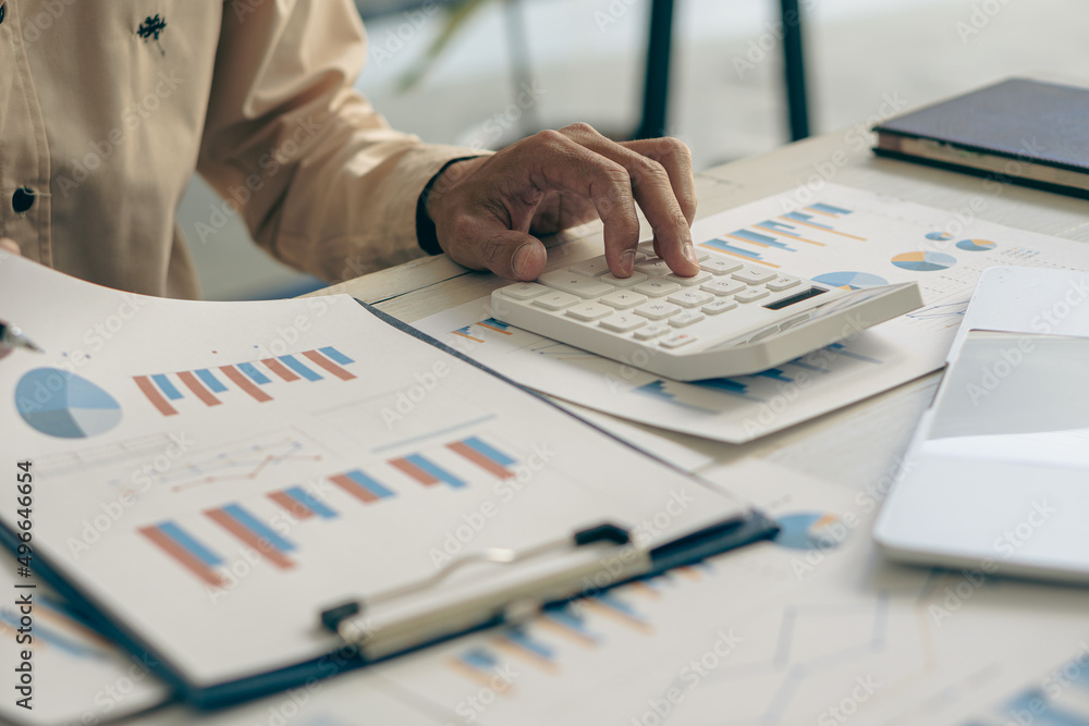 A businessman presses a calculator to calculate a price estimate with a laptop. Accountants make monthly financial reports or company profits at their desks. and the concept of working from home A businessman presses a calculator to calculate a price estimate with a laptop. Accountants make monthly financial reports or company profits at their desks. and the concept of working from home