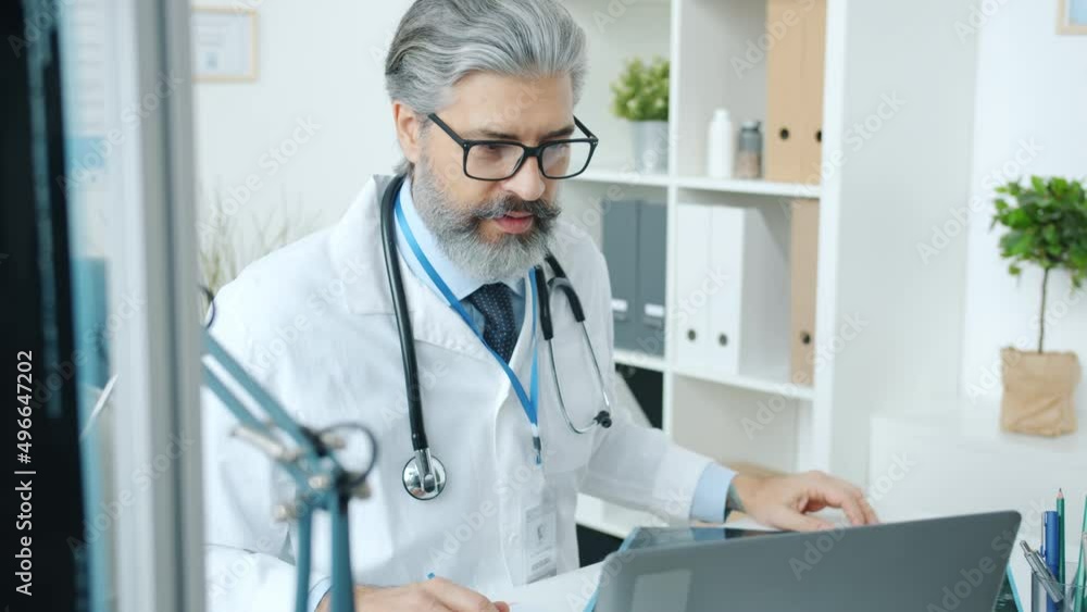 Mature doctor discussing MRI scan during online video consultation using laptop in office talking and looking at computer screen. Technology and healthcare concept. Mature doctor discussing MRI scan during online video consultation using laptop in office talking and looking at computer screen. Technology and healthcare concept.
