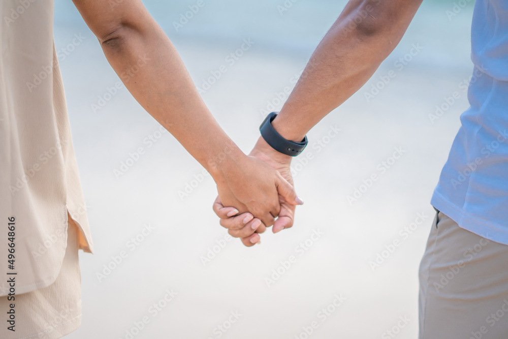 Hands of a woman and a man walking by the sea