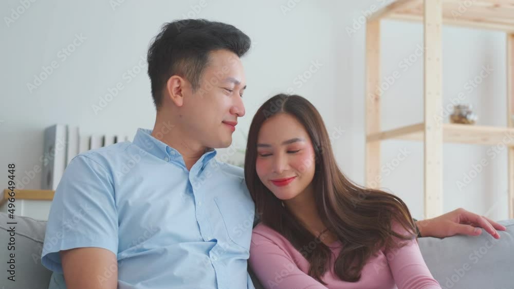 Young happy Asian couple sitting relaxing on sofa couch in living room. Woman leaning head on boyfriends shoulder. Asian couple man and woman talking working spend time together at home Young happy Asian couple sitting relaxing on sofa couch in living room. Woman leaning head on boyfriends shoulder. Asian couple man and woman talking working spend time together at home