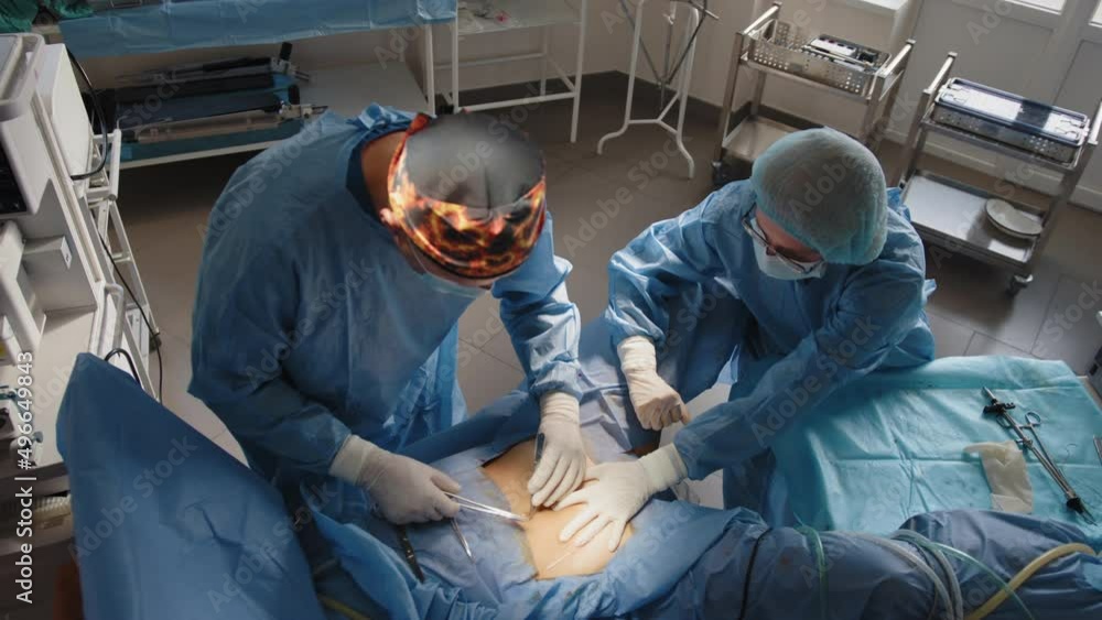 The surgeon uses a needle holder to hold the surgical needle and thread to suture the patient's skin. A team of surgeons stitches the patient's skin using a needle holder and surgical suture The surgeon uses a needle holder to hold the surgical needle and thread to suture the patient's skin. A team of surgeons stitches the patient's skin using a needle holder and surgical suture