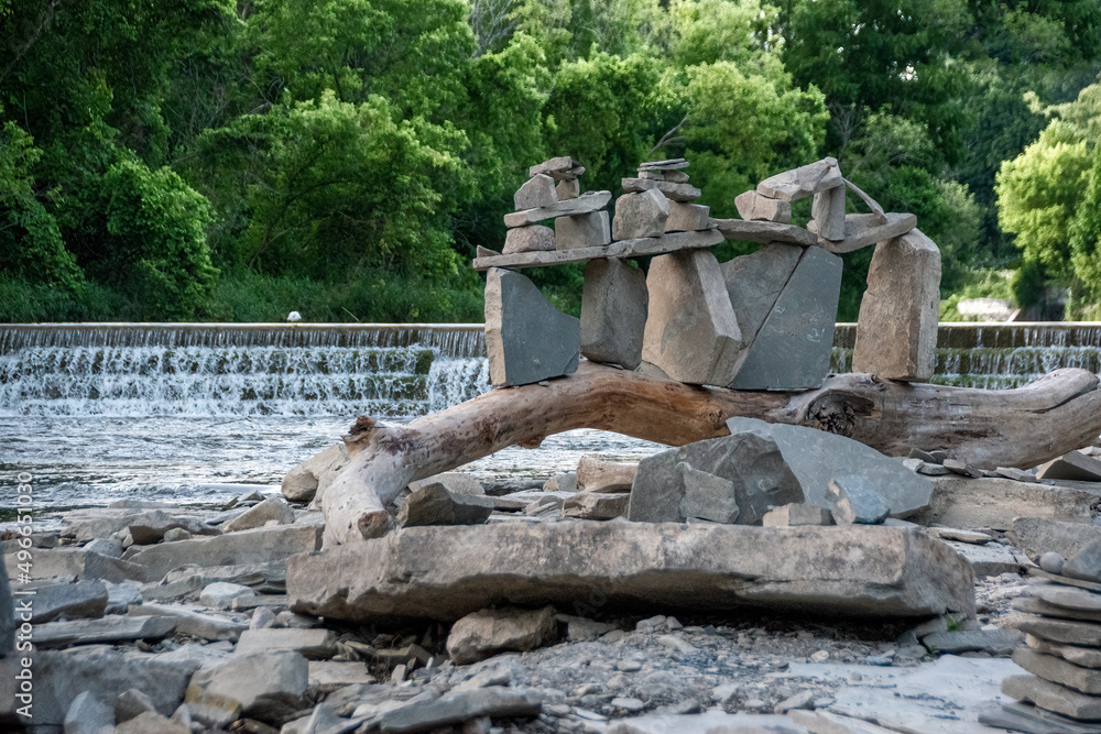 A group of rocks is stacked artistically on top of a curved log beside a river and small waterfall in Marie Curtis Park in Toronto, Ontario. A group of rocks is stacked artistically on top of a curved log beside a river and small waterfall in Marie Curtis Park in Toronto, Ontario.