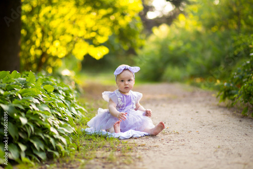 A little girl in a dress is sitting on the grass. summer walk with mom in the park  © urika