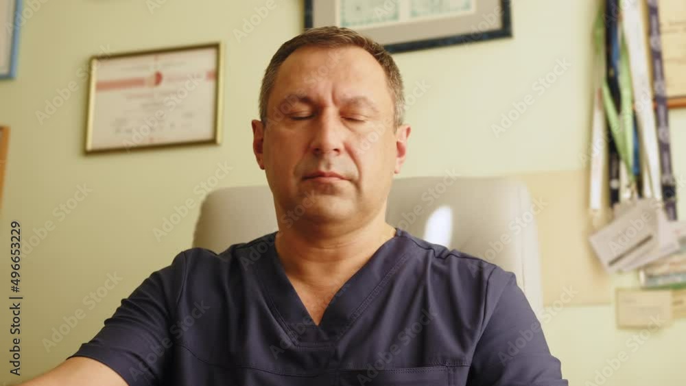Middle Aged Family Medical Doctor is Working in a Health Clinic. Successful Senior Physician. Portrait of handsome adult busy Caucasian male doctor sitting at desk in hospital office working. Middle Aged Family Medical Doctor is Working in a Health Clinic. Successful Senior Physician. Portrait of handsome adult busy Caucasian male doctor sitting at desk in hospital office working.