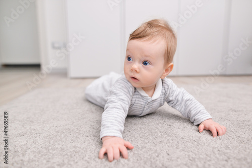 Charming newborn baby in a bodysuit lies on his stomach on a soft carpet. Laying out on the tummy. play, child development. space for text. High quality photo