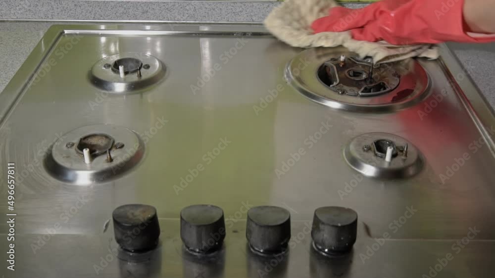 Woman in gloves washes and rubs a gas stove with detergent until it