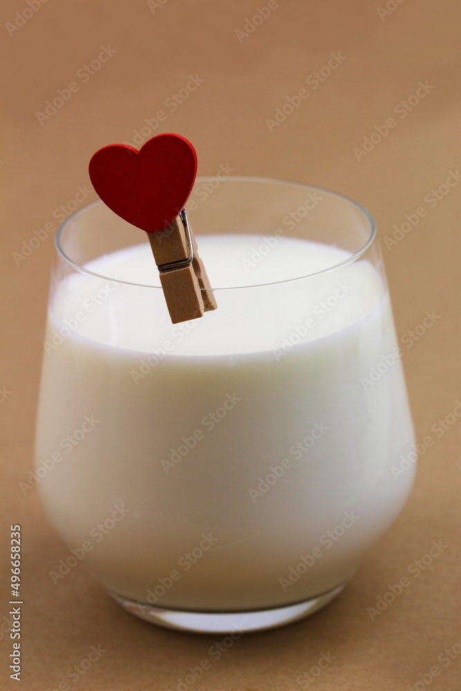 Fresh milk in transparent glass with red wooden heart on wooden paper clip