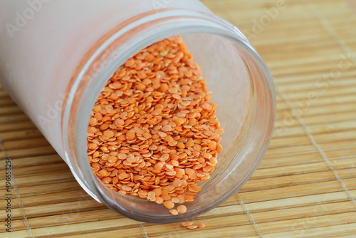 Uncooked red lentils in glass bottle on bamboo mat
