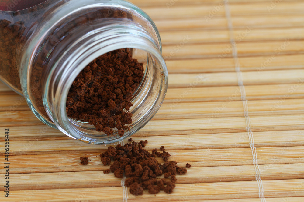 Granules of instant coffee scattered from transparent glass bottle