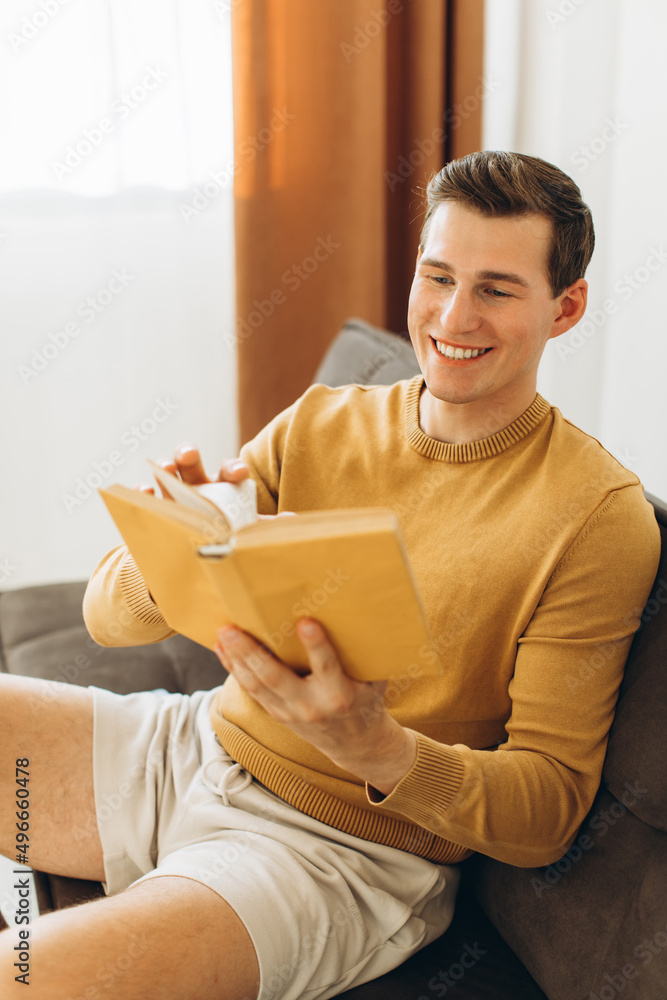 Handsome young man in yellow casual clothes sitting at home reading a book Handsome young man in yellow casual clothes sitting at home reading a book