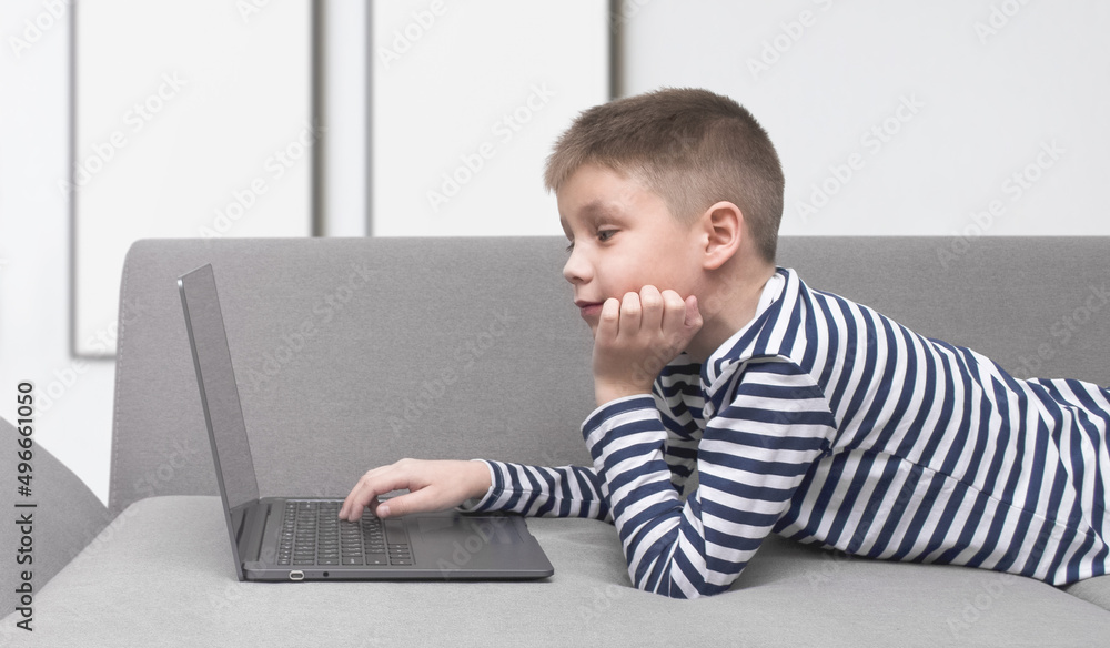 Child looking into an open laptop while lying on the couch Child looking into an open laptop while lying on the couch