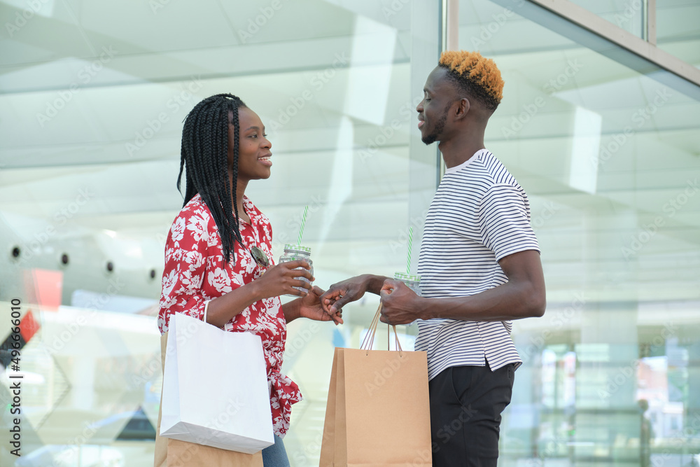 Young african couple drinking refreshing drinks and going shopping, holding hands. City life concept.