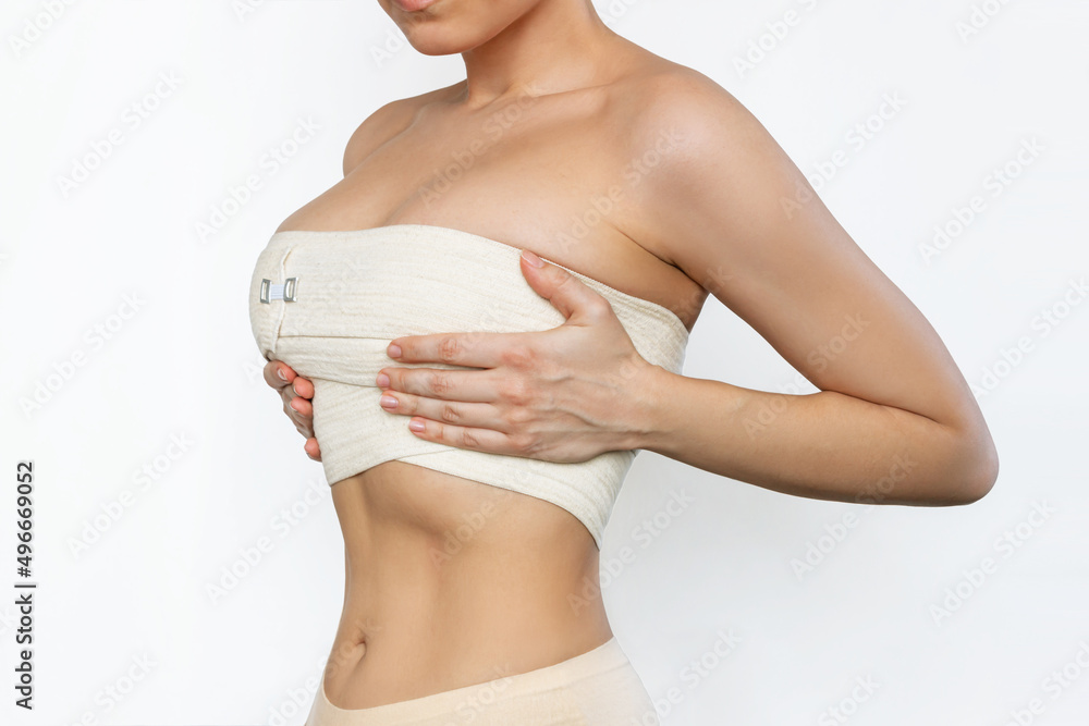 © Марина Демешко - Cropped shot of young fit woman wrapped in elastic bandage after breast augmentation isolated on white background. Result of lifting. Pain after plastic surgery. Girl is trying to hide her big breast © Марина Демешко - Cropped shot of young fit woman wrapped in elastic bandage after breast augmentation isolated on white background. Result of lifting. Pain after plastic surgery. Girl is trying to hide her big breast