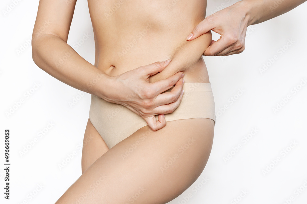 Cropped shot of a young woman holding fat fold on her side isolated on a white background. Overweight, flabby and sagging muscles. Body positive