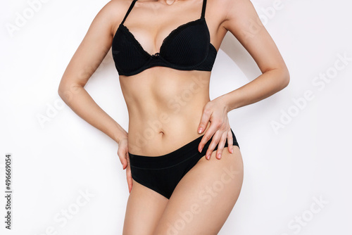 Cropped shot of young woman in black underwear demonstrating her slender figure with toned abs on stomach isolated on white background. Result of fitness, diet, healthy lifestyle. Female perfect body