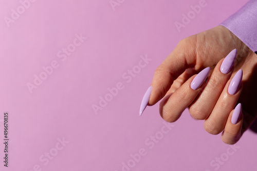 Female hand with a beautiful purple long nails manicure on a lilac background