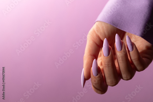 Female hand with a beautiful purple long nails manicure on a lilac background