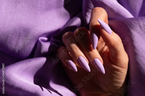 Girl s hand with an elegant manicure in a purple color on a purple silk background