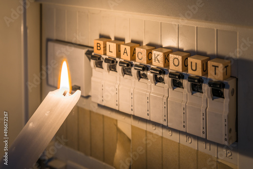Sicherungskasten mit Sicherungen in einem Verteilerkasten während eines Stromausfall mit weißer Kerze beleuchtet die ein Mann in der Hand hält mit dem Wort Blackout als Text, Deutschland photo