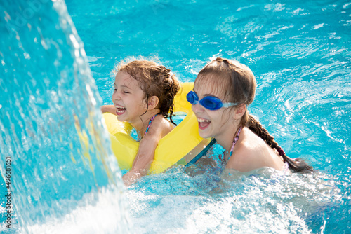 Two young smiling girls in a swimsuit bathes play in a pool with blue clear water in blue swimming glasses. Summer. Rest. Vacation.