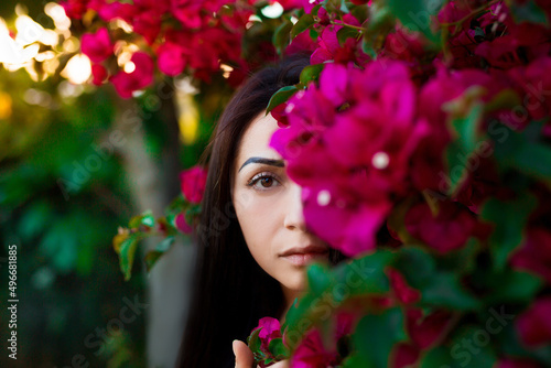 Close up portrait of a beautiful girl near colorful flowers. Pretty tender young woman model looking at camera.
