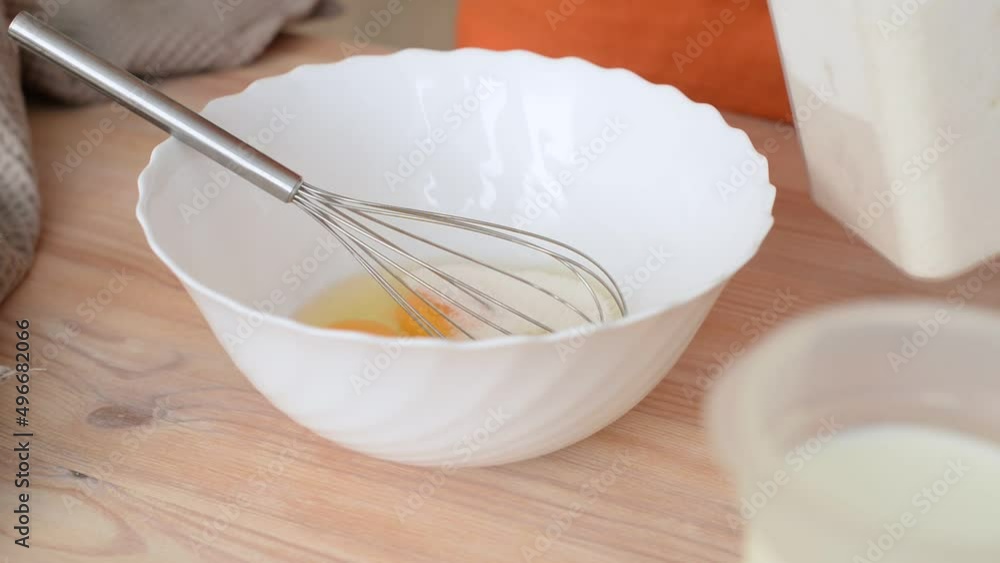 Female hands add sugar to eggs in a bowl and stir the mixture with a whisk, close-up Female hands add sugar to eggs in a bowl and stir the mixture with a whisk, close-up