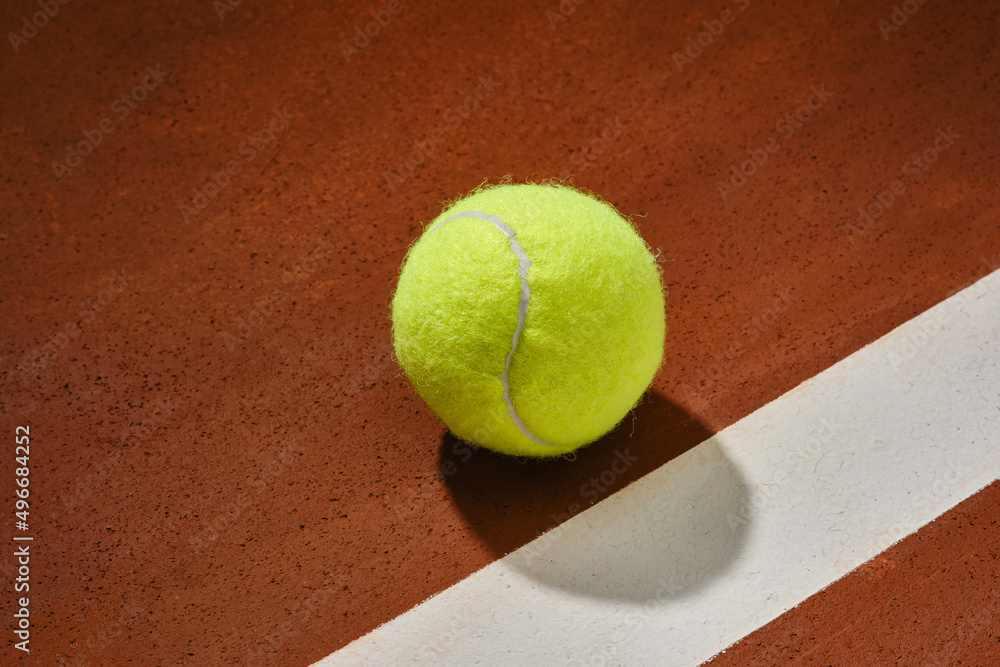 Tennis ball on a orange court surface with white stripe. Shallow depth of field