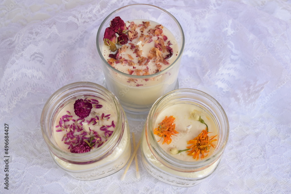 Hand-poured scented soy candles with dried flowers on table with lace. Hand-poured scented soy candles with dried flowers on table with lace.