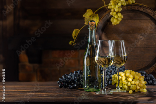 Glass of wine, bottle of wine, grape in front of the rustic barrels for beverage in a dark wine cellar. Wooden empty surfaces for copy space, mock up, template for design of wine, alcohol products