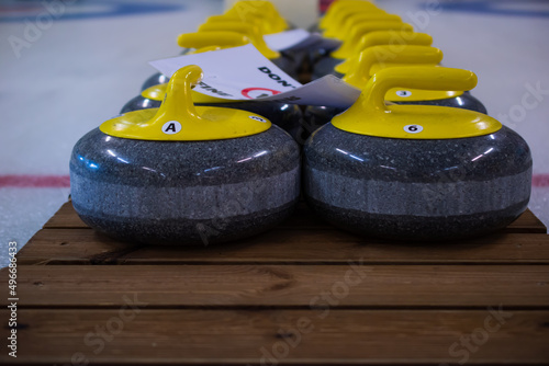 Curling stones with a yellow handle sit on a wooden base.