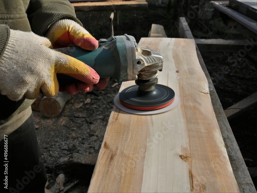 smoothing the surface of a wooden board with an emery disc on a grinder in the hands of a carpenter, processing a wooden material with a grinder with an emery nozzle