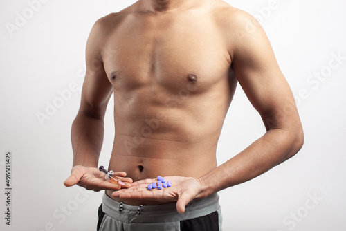 shirtless fitness muscular man holding anabolic steroid syringe and multivitamin supplement pills on palm