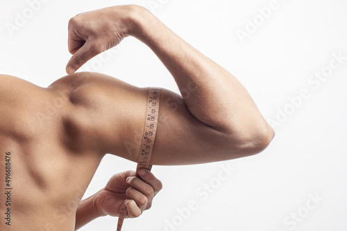 Young muscular man measuring his bicep with a tape measure isolated on white background.