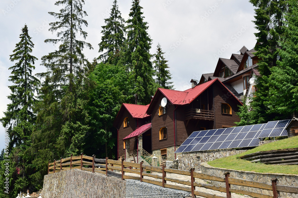 Cottages in a mountain forest near which rows of solar panels for renewable electricity