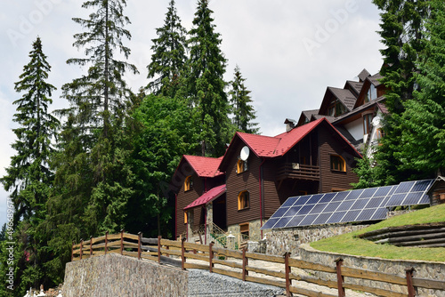 Cottages in a mountain forest near which rows of solar panels for renewable electricity