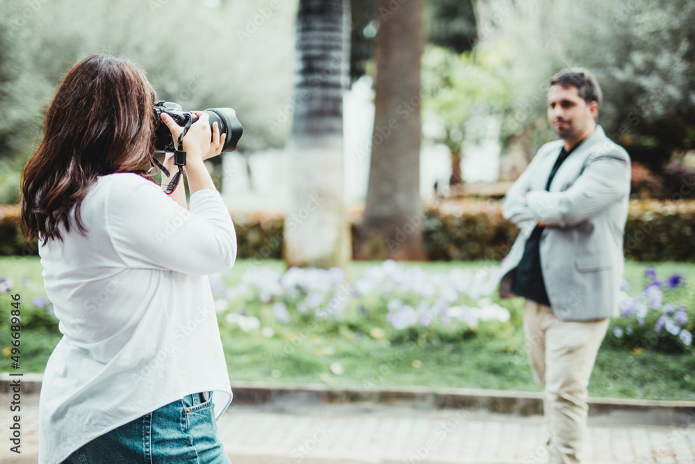 Selective focus on a woman taking a photo with a reflex camera to a businessman in a park Selective focus on a woman taking a photo with a reflex camera to a businessman in a park