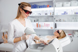 Smiling woman using laser epilation machine in beauty salon
