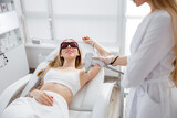Smiling woman receiving laser epilation treatment in beauty salon