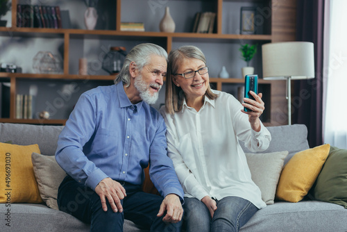 Elderly couple of senior retirees Happy gray haired grandparents communicate online in a video call using a mobile phone smartphone. laugh and wave hands. mature couple Remote meeting with children