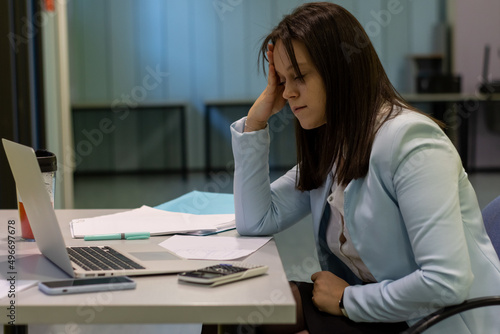 Tired businesswoman working with a laptop and touching her forehead, she is exhausted and having an headache, stressful job concept