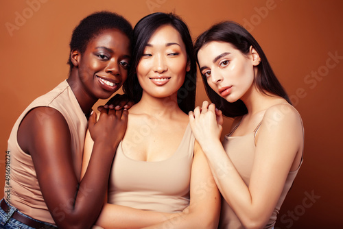 young pretty asian, caucasian, african woman posing cheerful together on brown background, lifestyle diverse nationality people concept