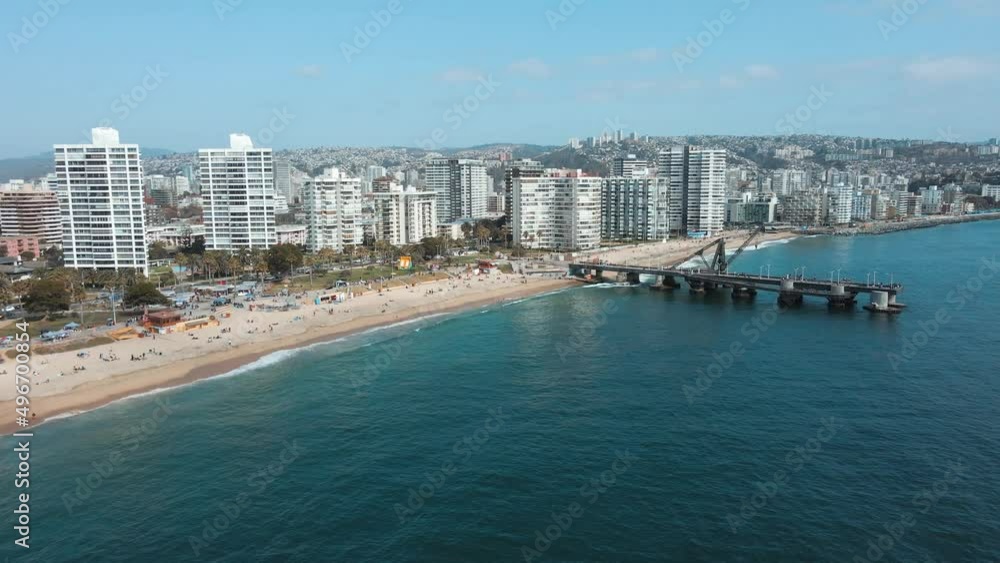 Aerial truck right of Vergara pier and crane in turquoise sea near El Sol beach sand shore, Viña del Mar buildings in background, Chile Aerial truck right of Vergara pier and crane in turquoise sea near El Sol beach sand shore, Viña del Mar buildings in background, Chile