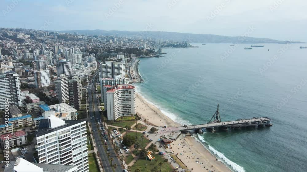 Aerial truck right of El Sol beach shore and turquoise sea near Vergara pier and crane, Viña del Mar buildings in background, Chile Aerial truck right of El Sol beach shore and turquoise sea near Vergara pier and crane, Viña del Mar buildings in background, Chile